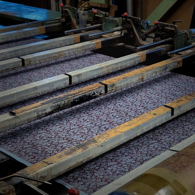 プリント機にセットされたリバティ柄のリネン生地、何度もテストを重ねる自然なリネンに再現する調整の工場風景