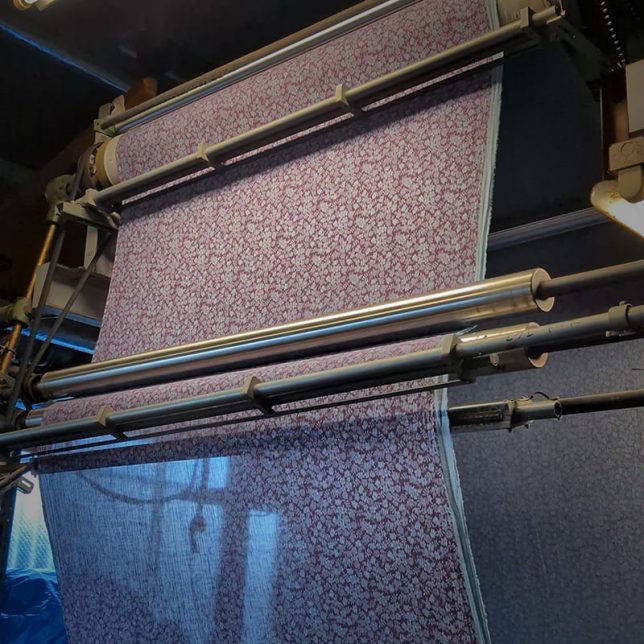 プリント機にセットされたリバティ柄のリネン生地、何度もテストを重ねる自然なリネンに再現する調整の工場風景